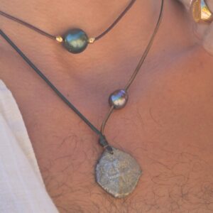 Leather necklace with a Spanish eight-reales coin and an off-centre pearl, close-up on the model.