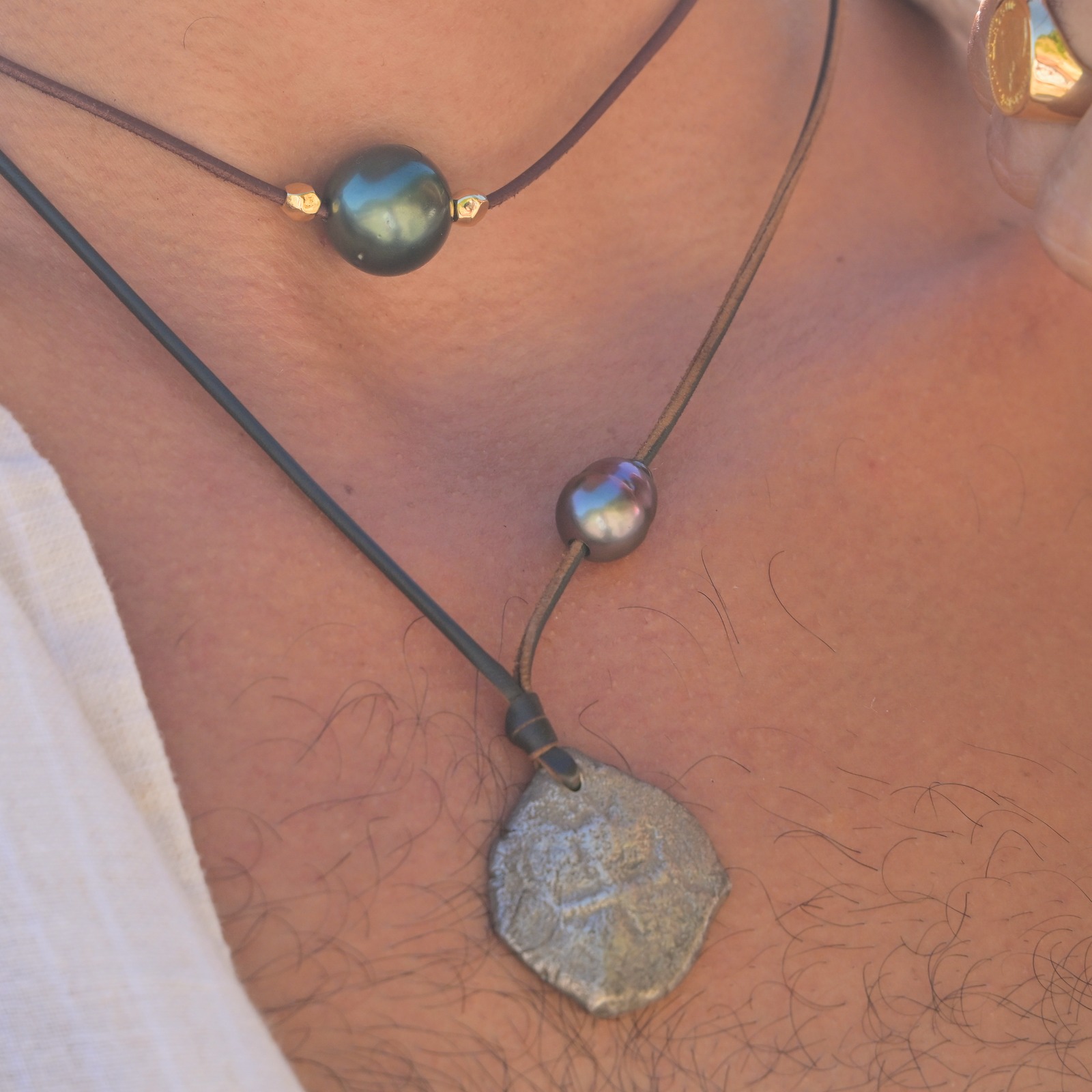 Leather necklace with a Spanish eight-reales coin and an off-centre pearl, close-up on the model.