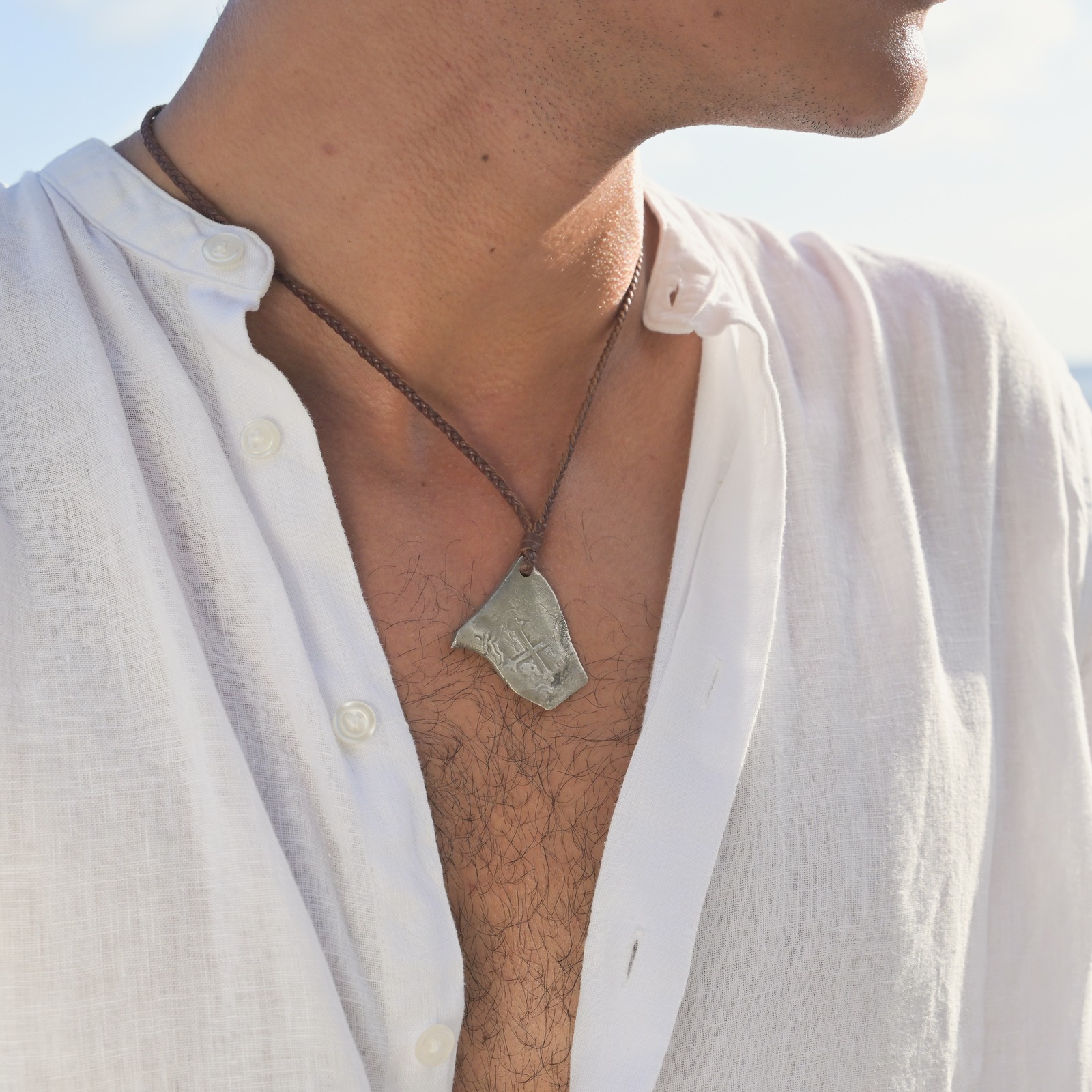 Braided leather necklace with a silver shipwreck coin, worn view.