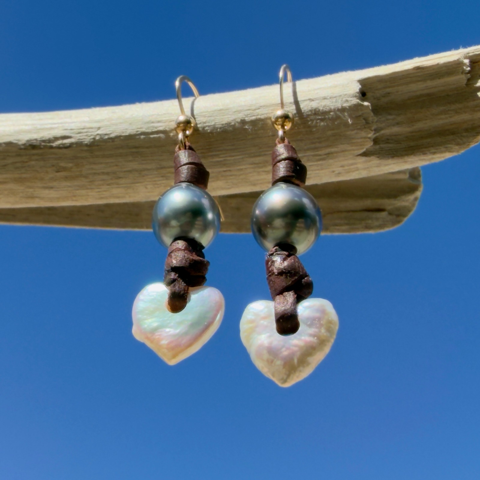 Boucles d’oreilles en cuir, cœurs en nacre et perles de Tahiti, posé en ambiance naturelle