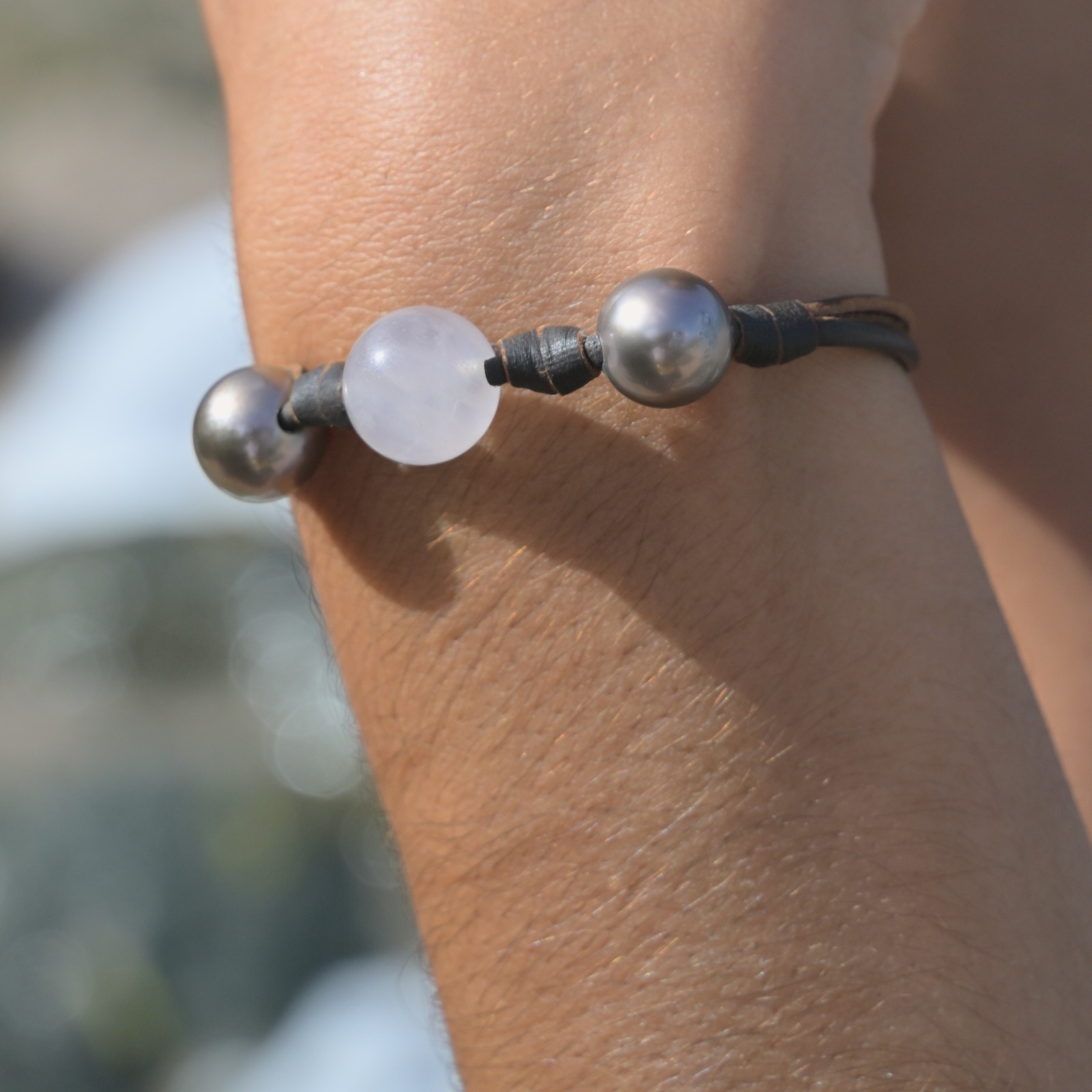 Leather bracelet with rose quartz between two Tahitian pearls, worn on the wrist