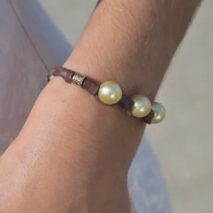 Leather bracelet with three golden pearls and golden tubes, worn on the wrist