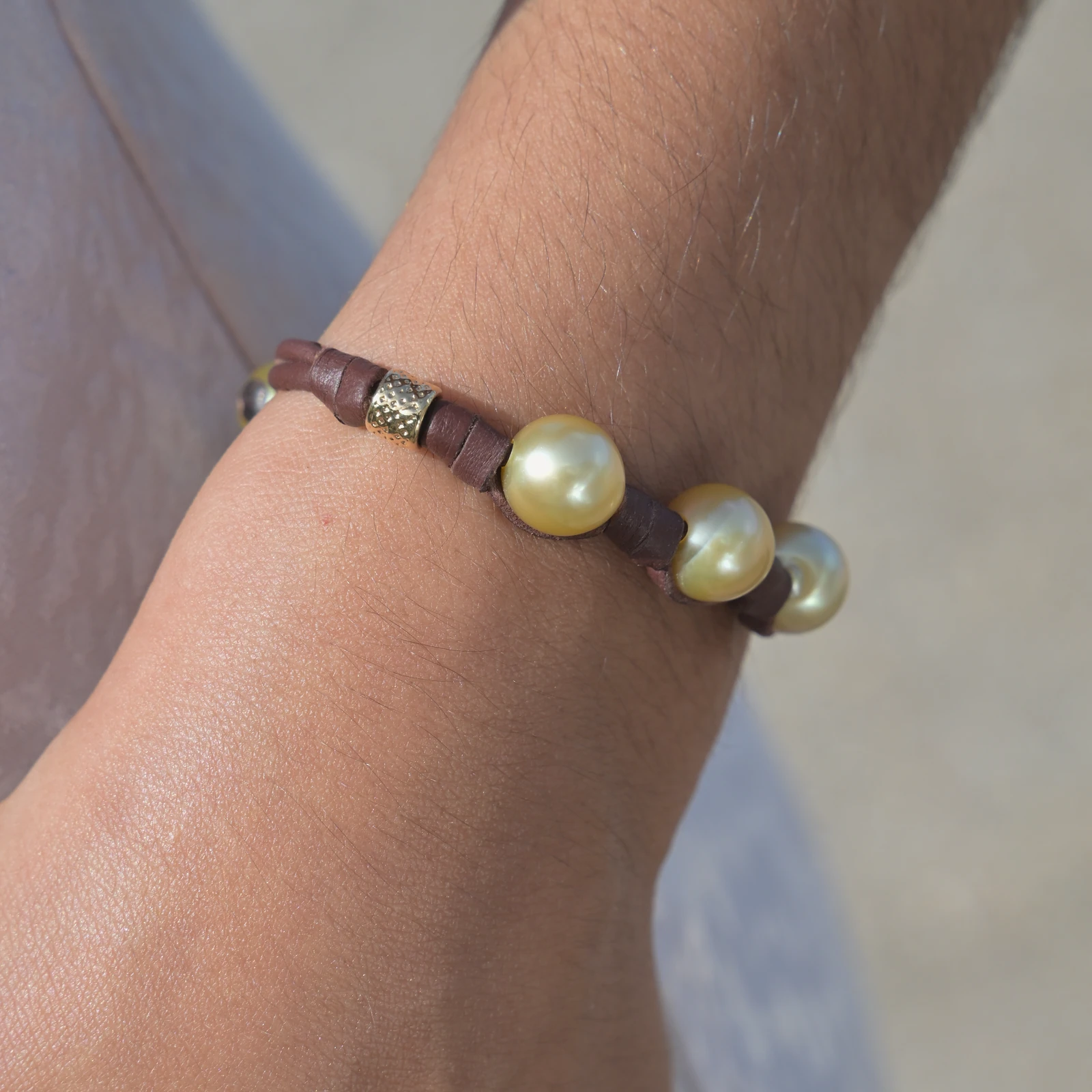 Leather bracelet with three golden pearls and golden tubes, worn on the wrist