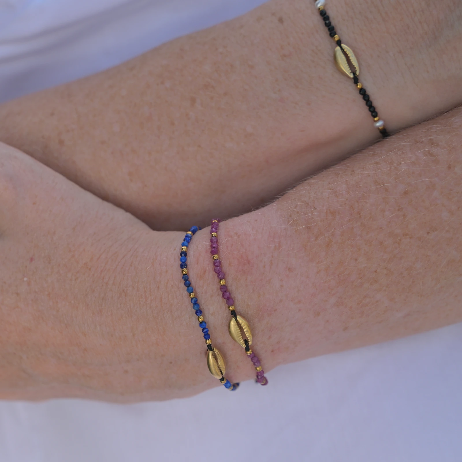 Adjustable bracelet with a gold-plated cowrie and faceted gemstones, worn
