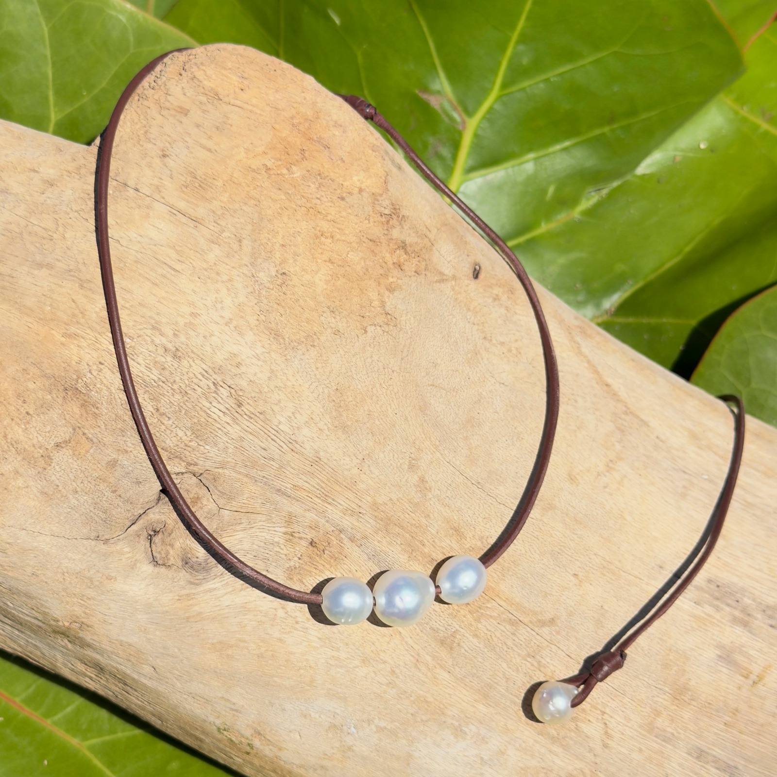 Collier ras du cou en cuir et trio de perles blanches baroques, bijou posé sur un fond naturel