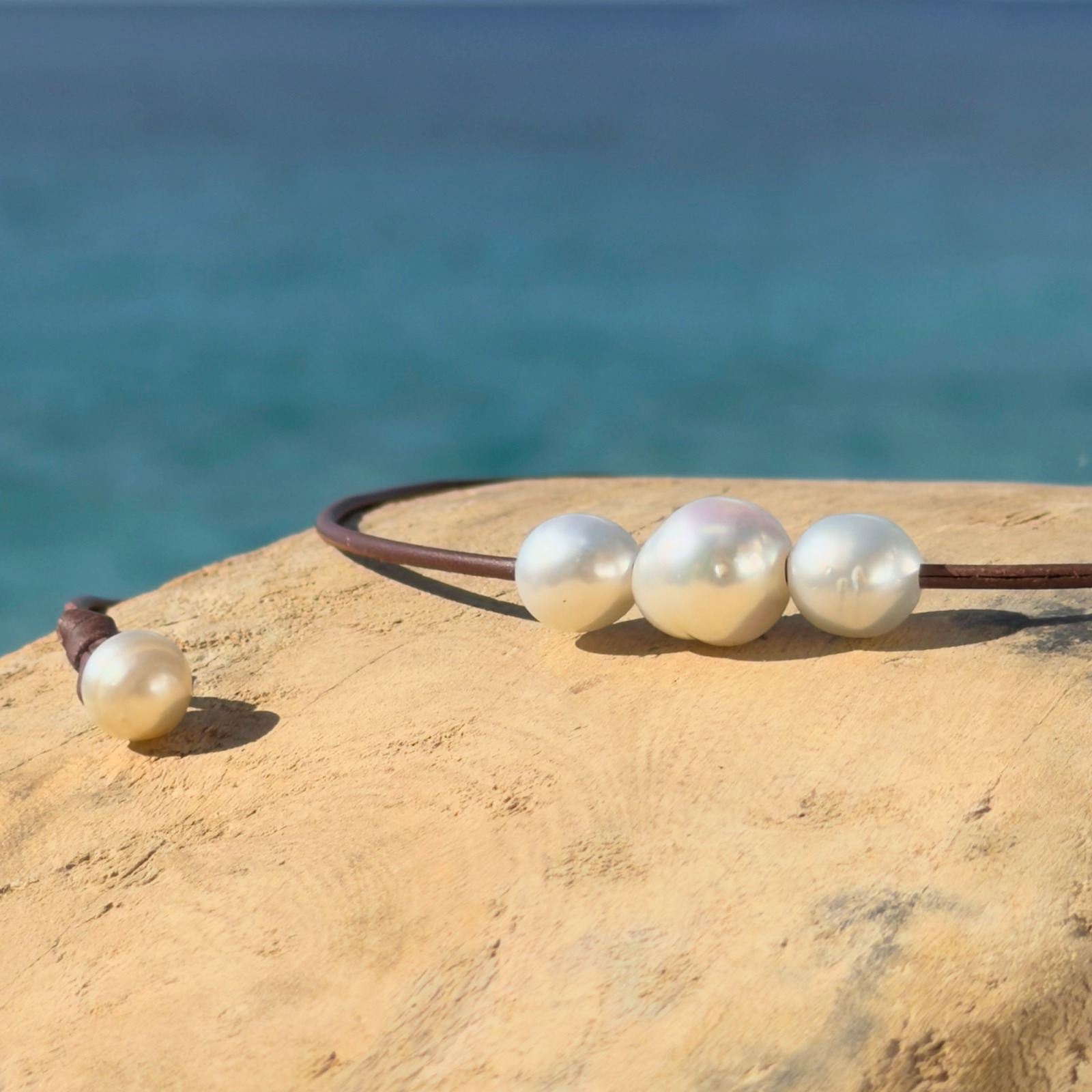 Collier ras du cou en cuir et trio de perles blanches baroques, bijou posé sur un fond naturel
