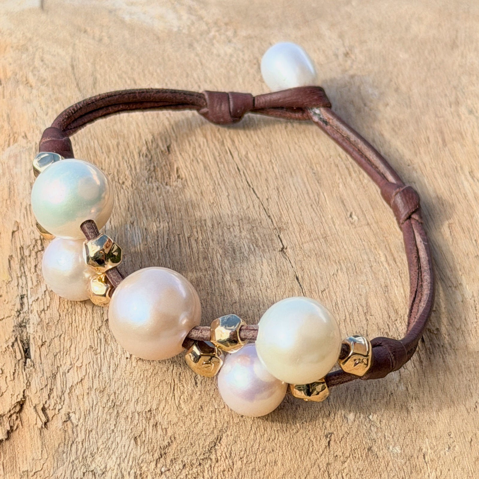 Bracelet Papillon en cuir, perles blanches et billes dorées, bijou posé sur un fond naturel